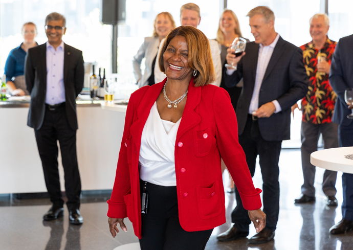 A woman wearing a red jacket is applauded by her colleagues during a meeting.