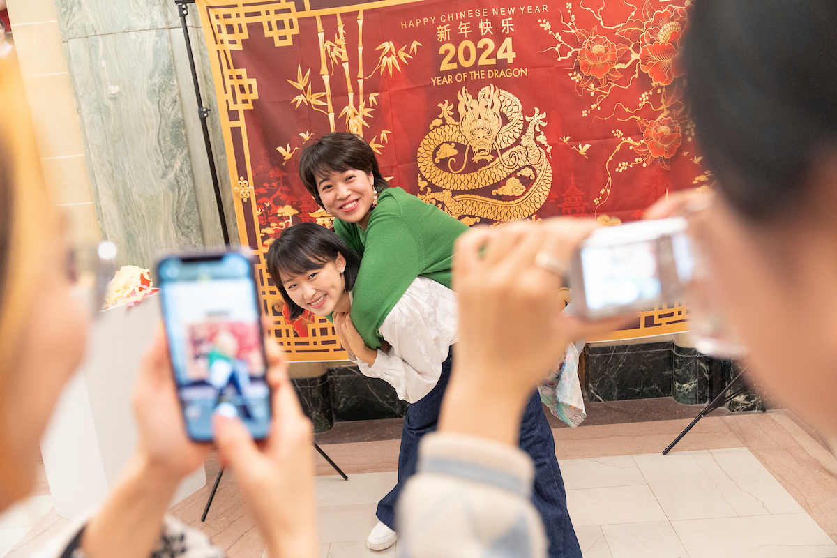 Two students posing for a picture with one on the back of the other with two other people taking photos. 