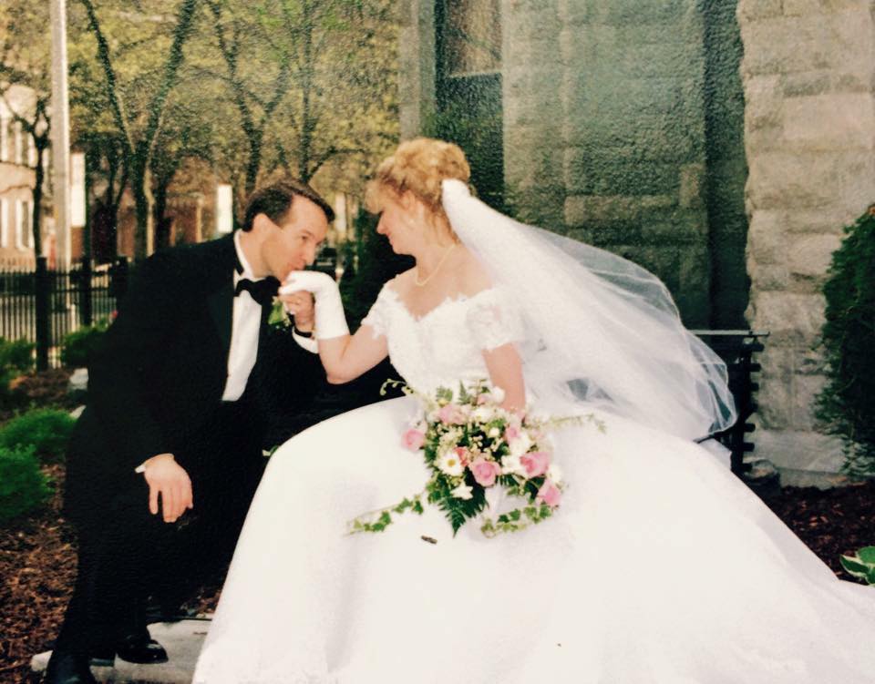 Bride and groom sitting on a park bench and the groom is kissing the bride's hand