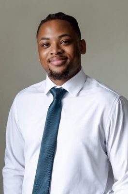 A man stands and smiles while posing for a headshot.