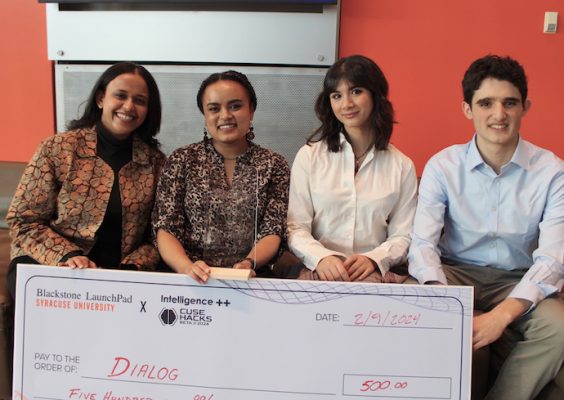 Four students pose indoors with an oversized check after winning the No Code Design Sprint competition.