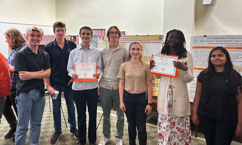 A group of high school students and SU affiliates pose together in front of research posters