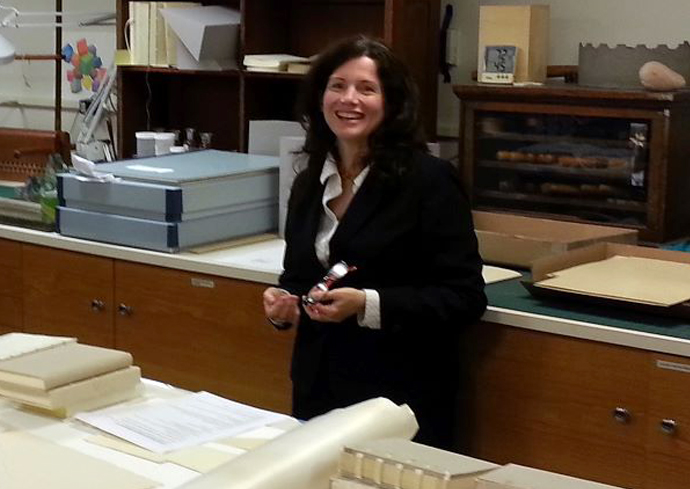 A woman smiles while standing in front of a collection of preserved texts.