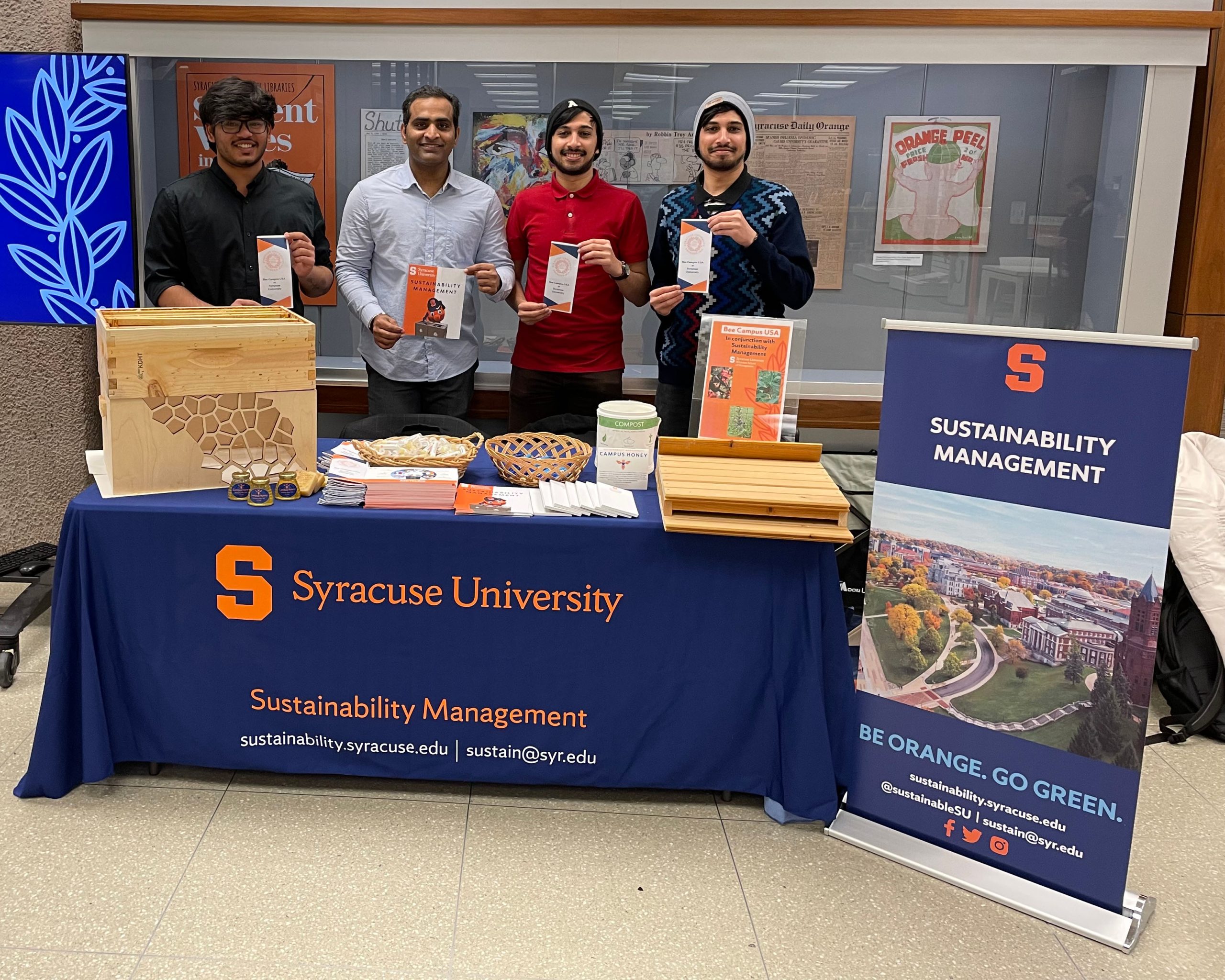 FOur people standing holding papers behind a sustainability management table in the Library.