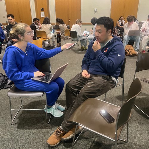 A student interviews another student in a classroom.