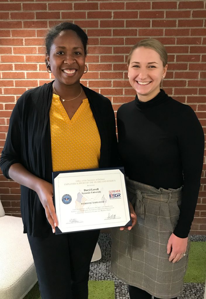 Two people standing together smiling with one person holding an award