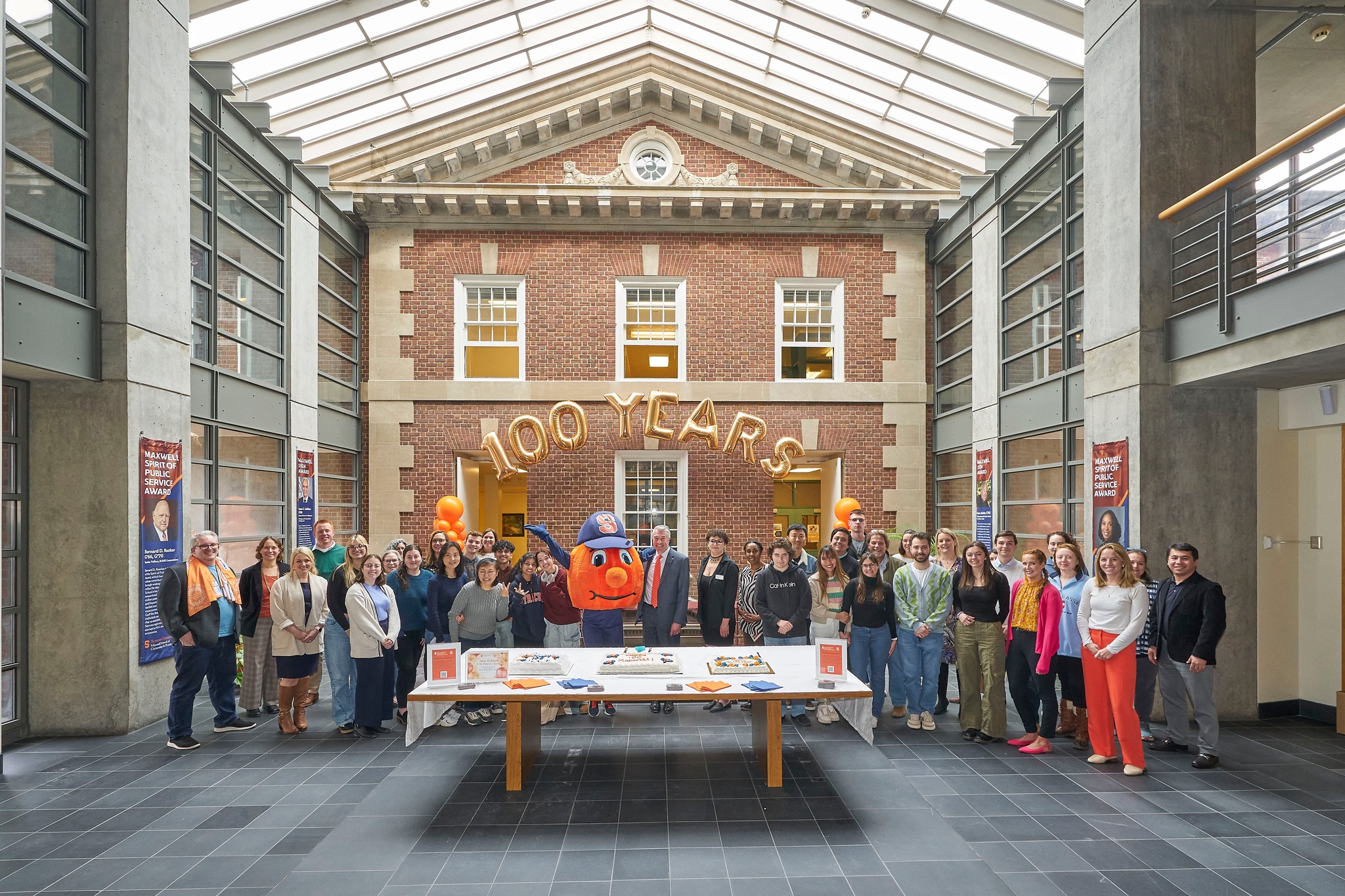Large group of people standing together for a photo with balloons in the background that says 100 years