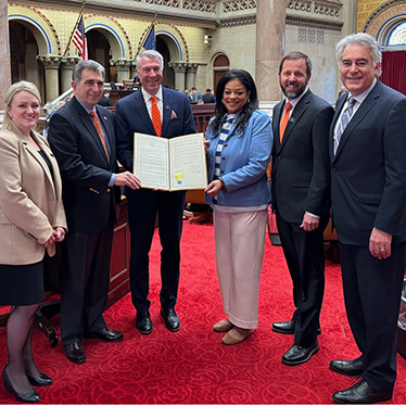 Group of people standing together posing for a photo with two individuals holding a government document.