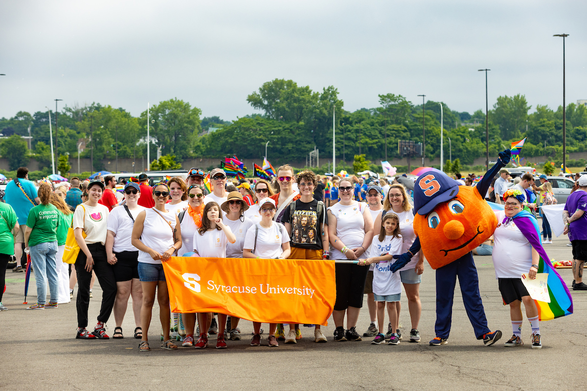 Large group of people gathered together for a photo holding an orange Syracuse University banner. 