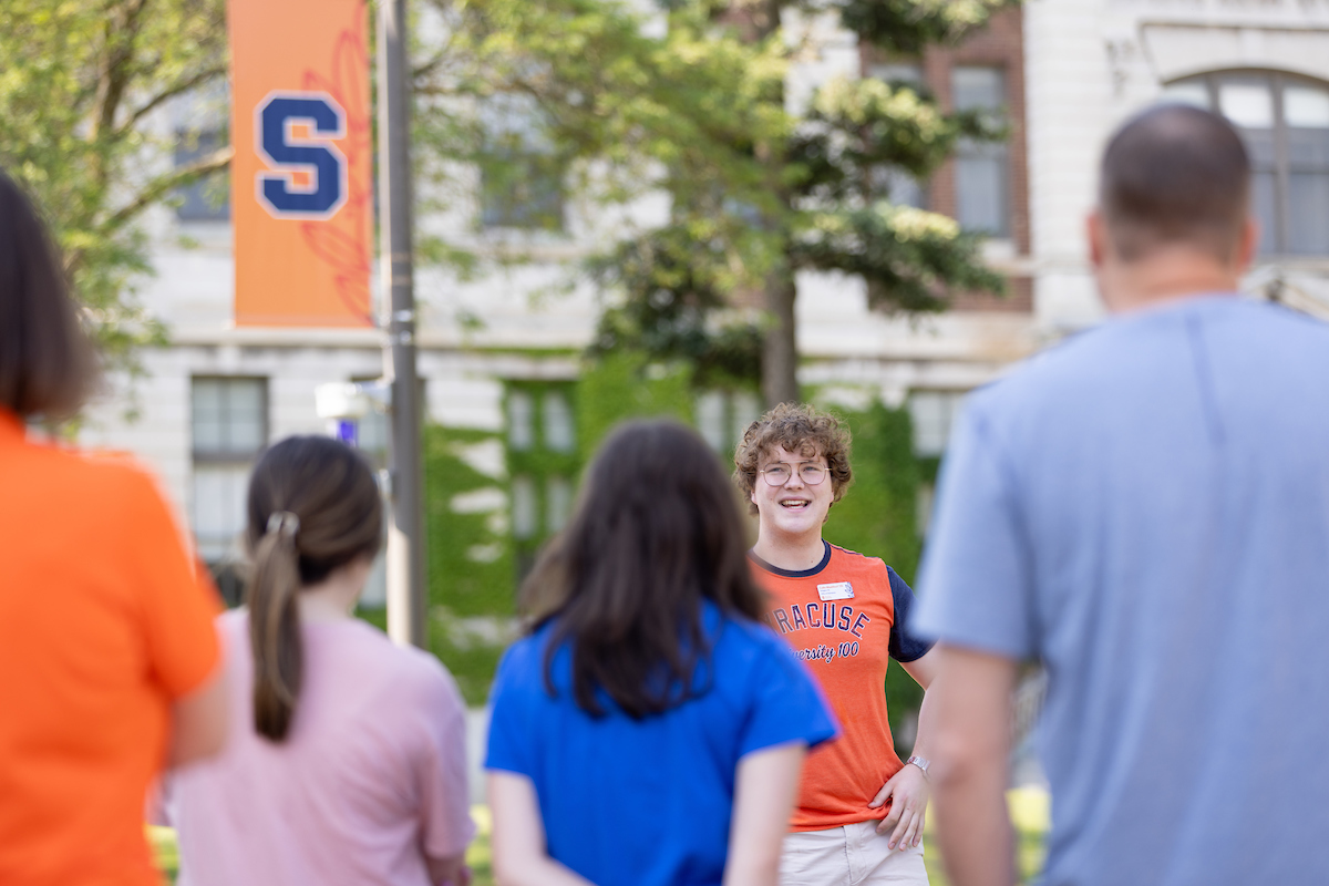 Person speaking to a group of people outside while giving a tour on campus 