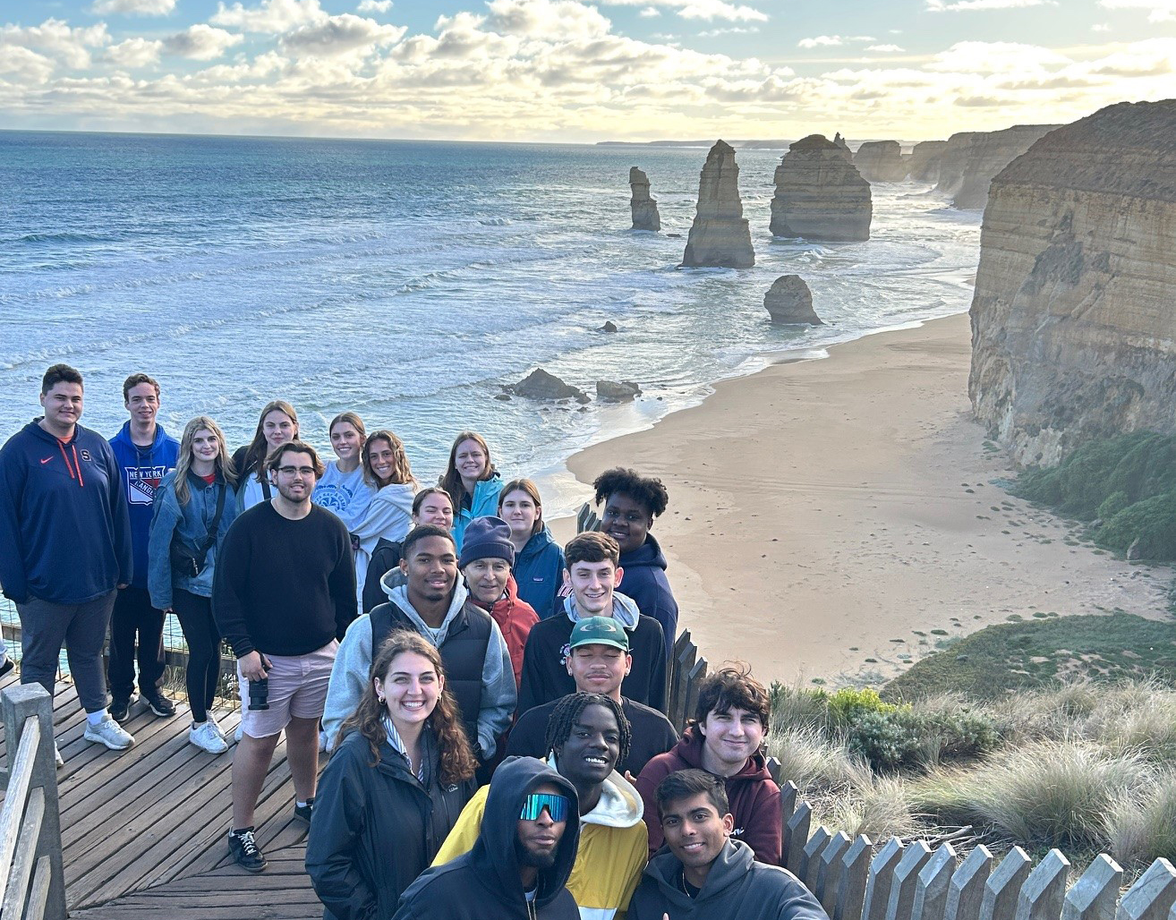 large group of students standing together on a set of stairs with the beach in the background