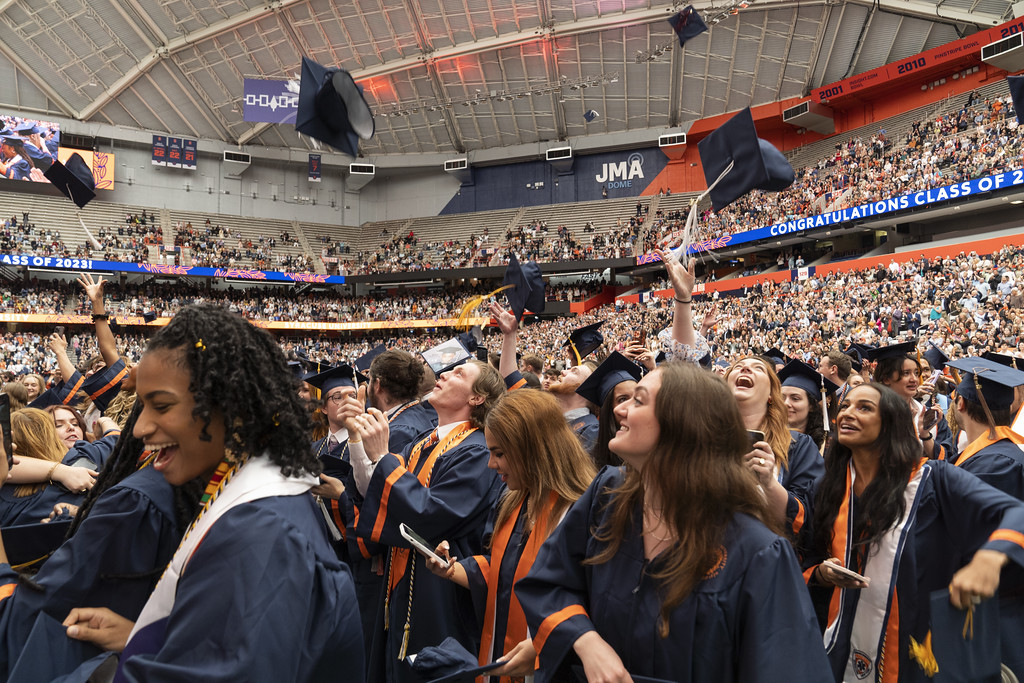 graduates in the JMA Wireless Dome throw up their caps during Commencement