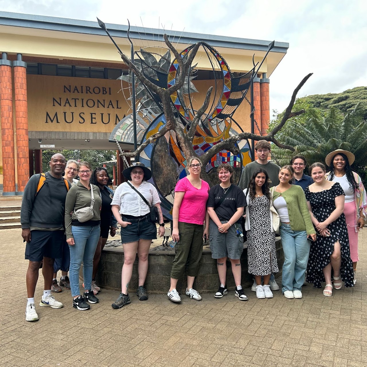 Group of people standing together in front a sculpture. 