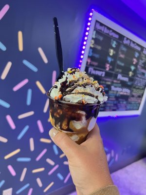 Hand holding up an ice cream sundae with chocolate sauce, whipped cream and resees pieces on top.