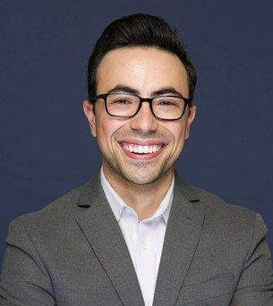 A man smiles while posing for a headshot indoors.