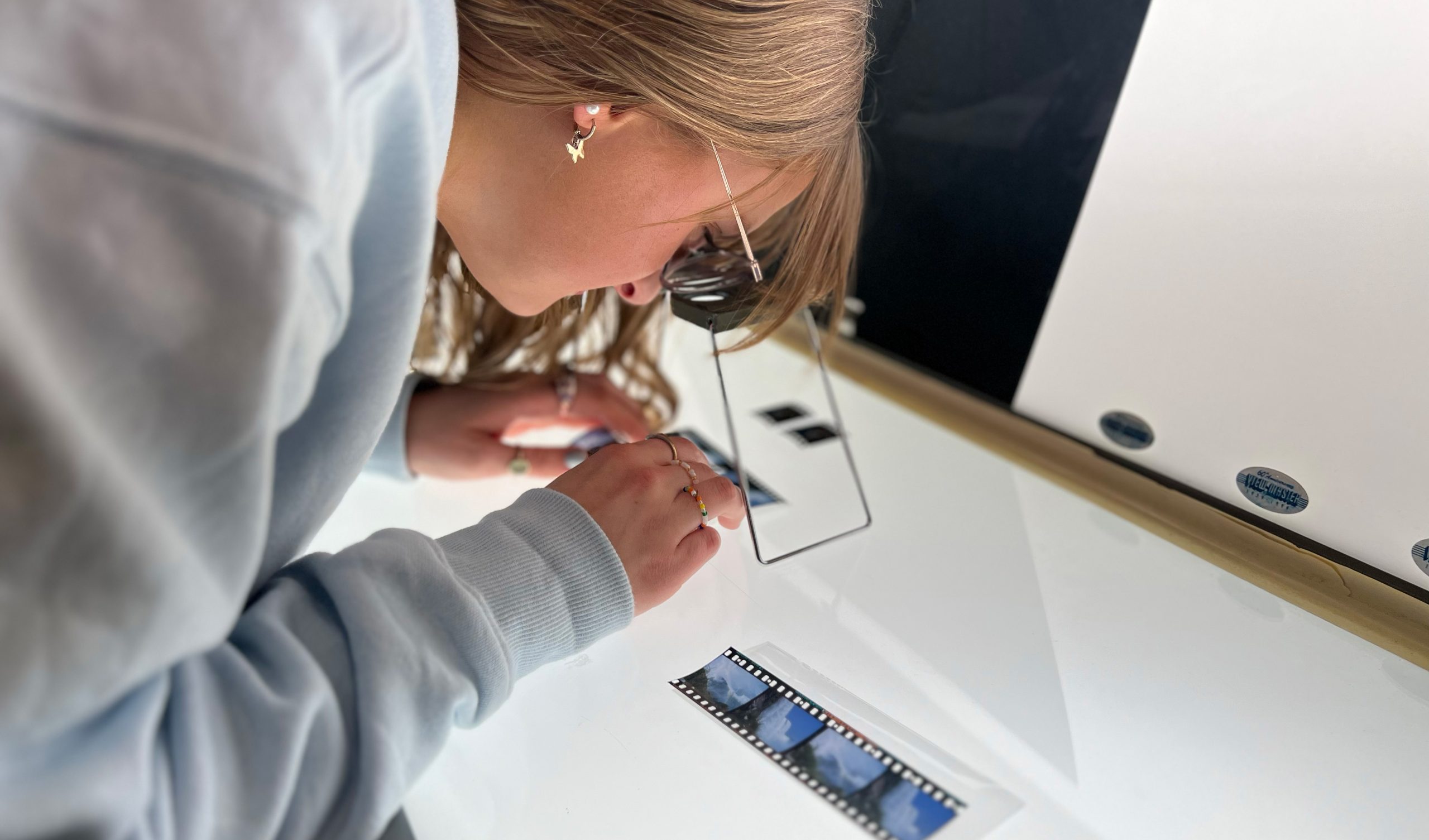 Student examines color positive film shot for stereoscopic viewing on a table that was illuminated with light.
