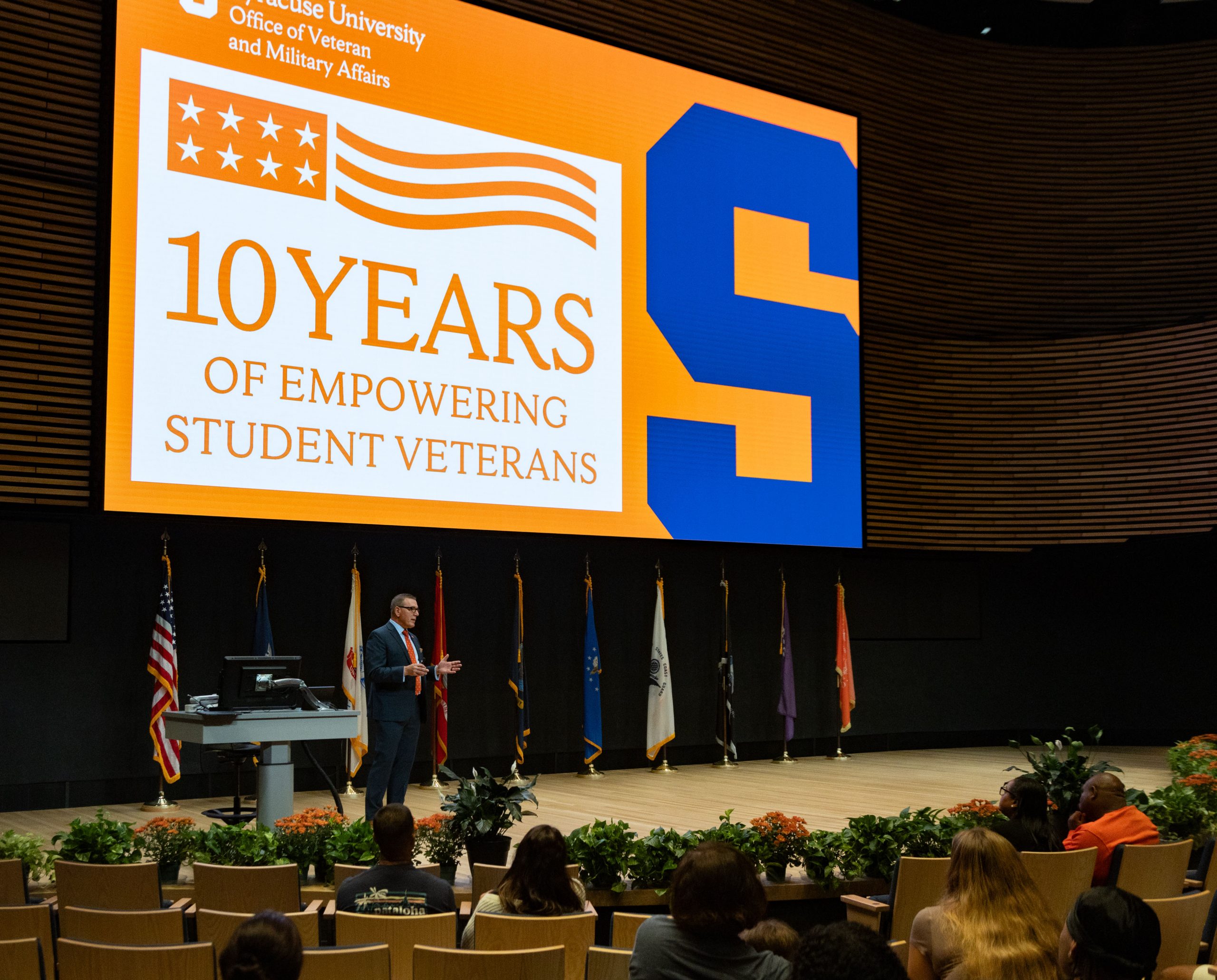 Person standing on a stage speaking with the large screen behind them that says 10 years of empowering student veterans