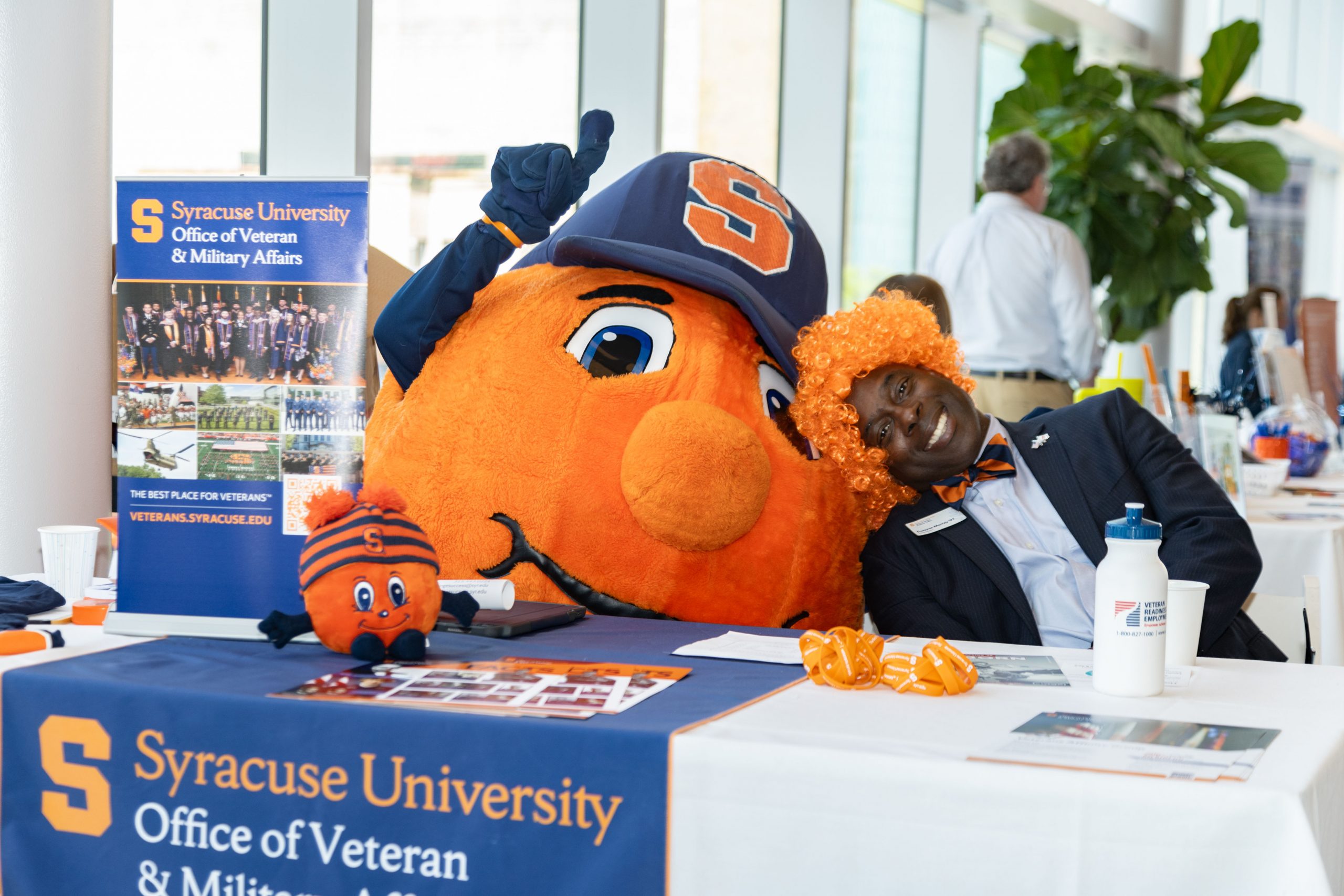 Person in orange wig sitting next to Otto the Orange at a table
