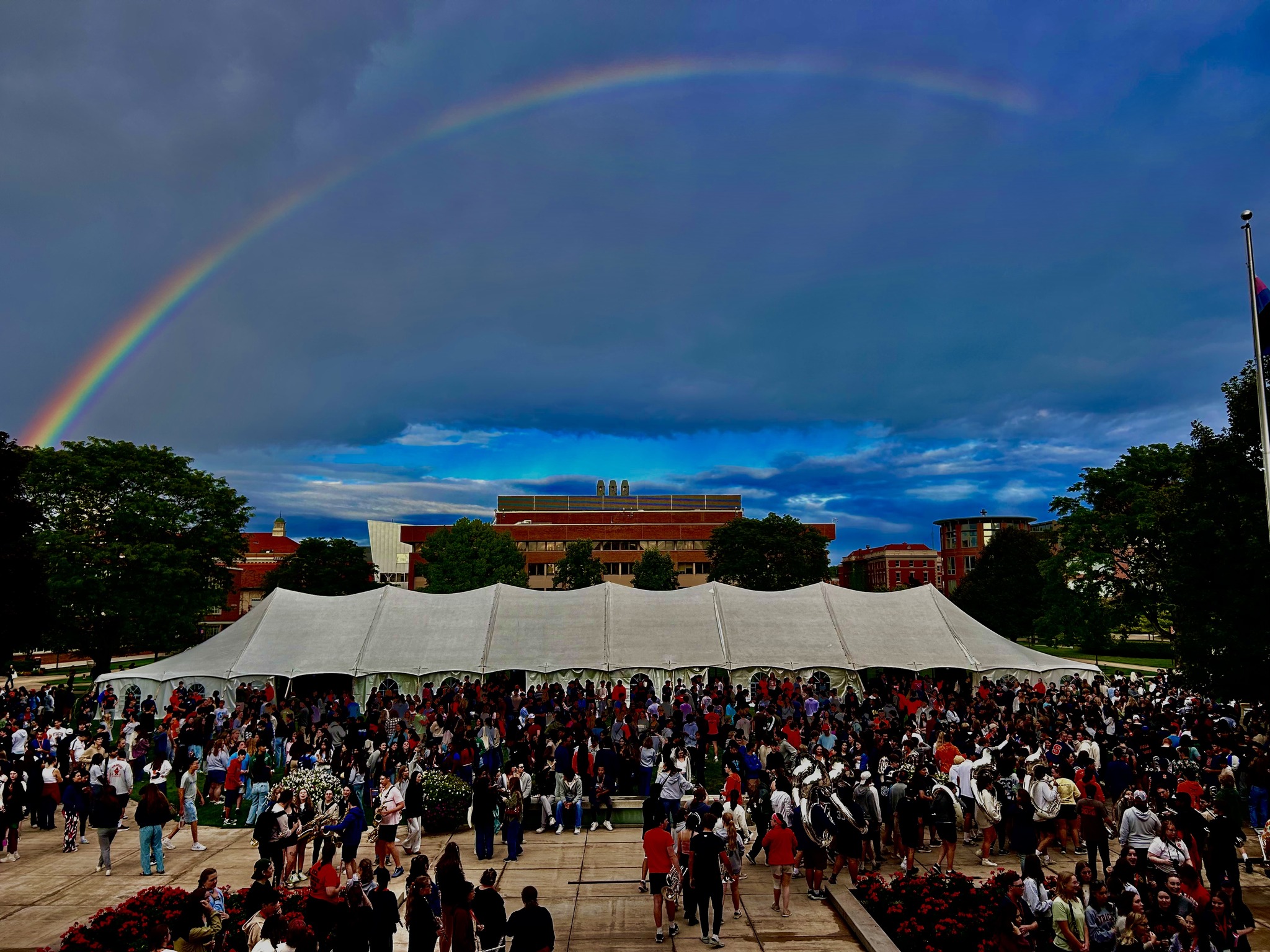 Rainbow over the Quad with a large white tent and a large group of people.