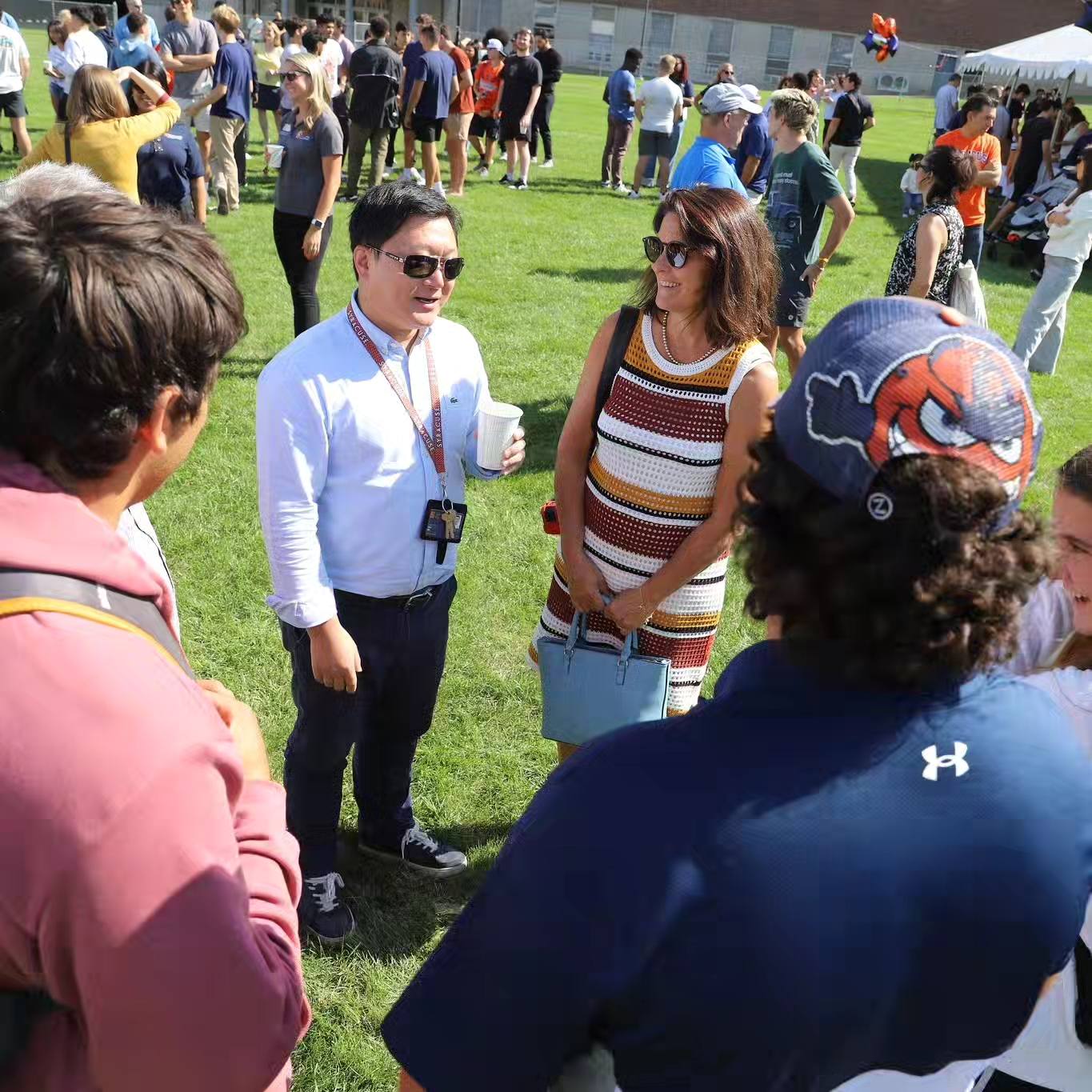 Group of people standing outside in the grass on a sunny day talking