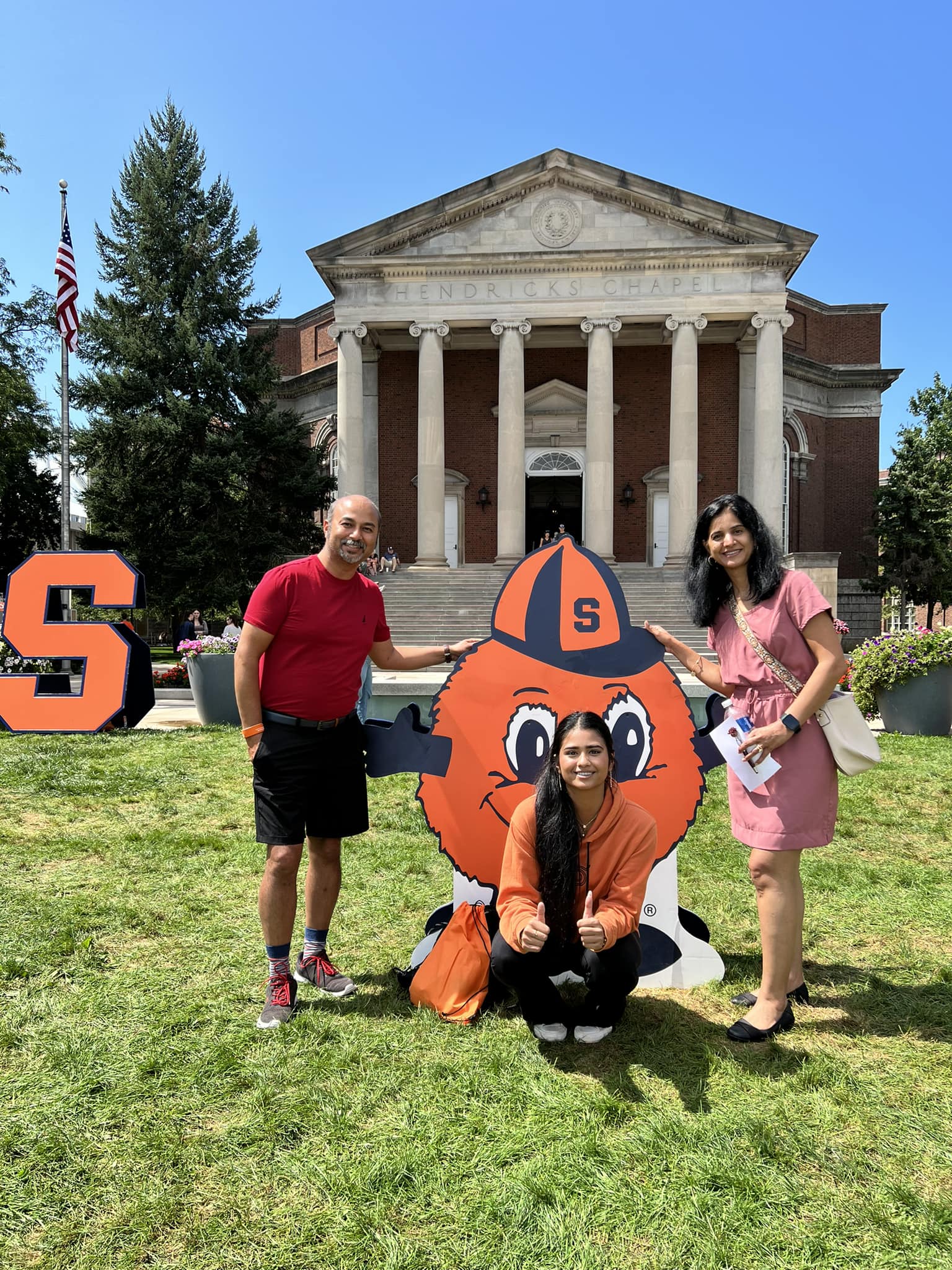 Three people standing on the quad with an Otto the Orange sign. 