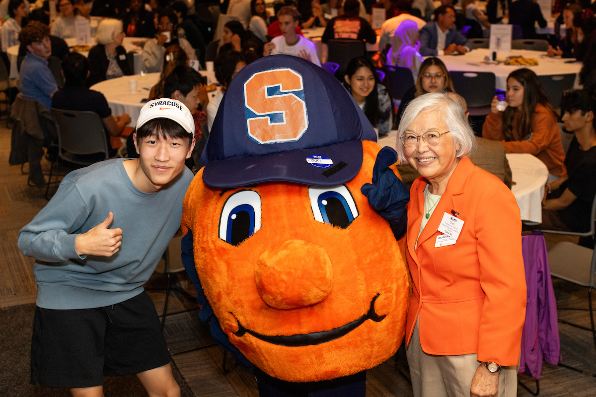 Two people standing with Otto the Orange