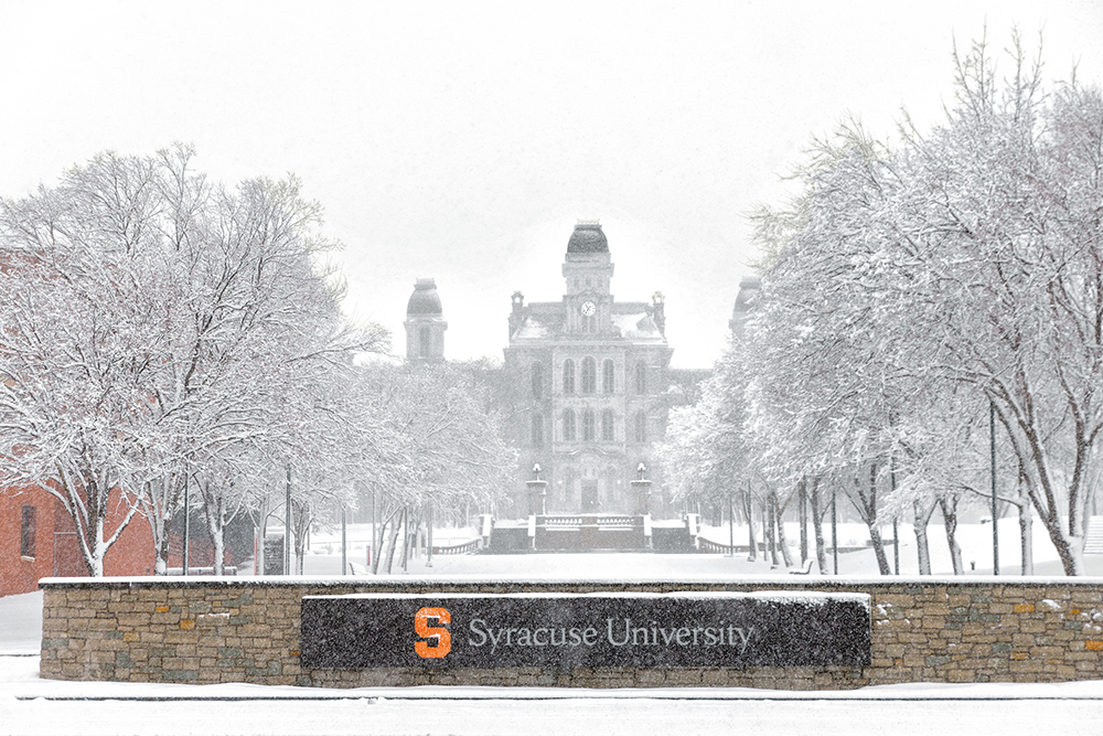 the Hall of Languages, multiple campus trees and Syracuse University sign in a light dusting of snow