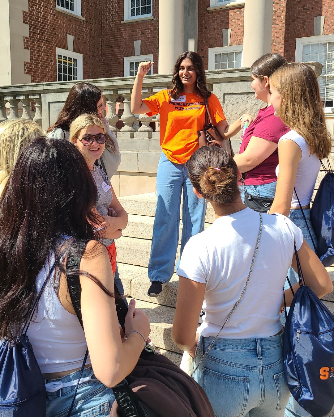 Student in Orange t-shirt talking to a group of students. 