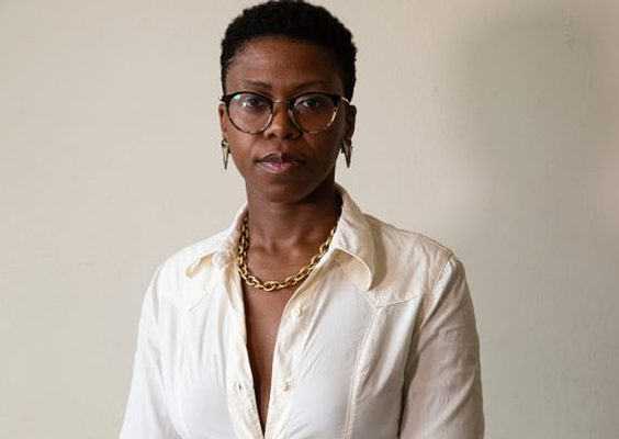A woman poses for a headshot in front of a white wall.