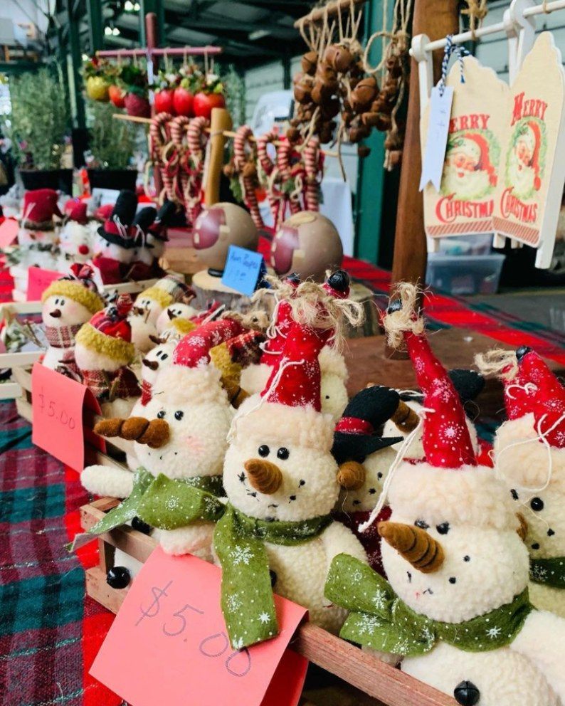 St￭ snowman toys wearing festive hats are displayed for sale at a market stall, with prices labeled in front. Decorative items and garlic braids hang in the background.