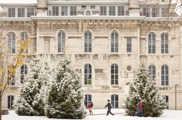 Students walking past a building on a snow-covered day on the Syracuse University campus.