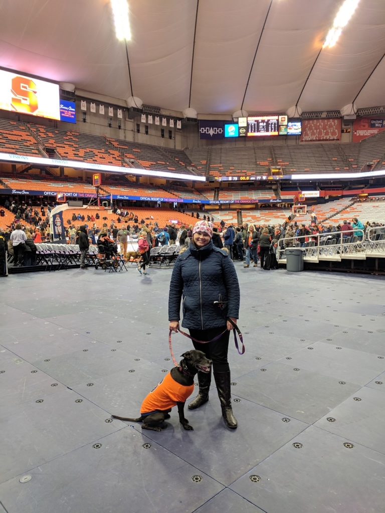 Woman stands with dog inside arena.