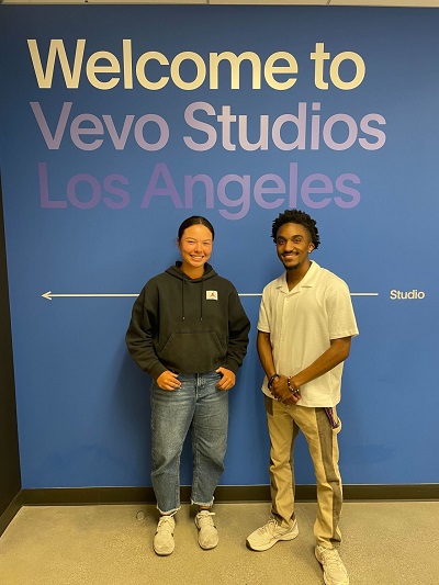two people standing in front of a wall that says Vevo Studios, Los Angeles