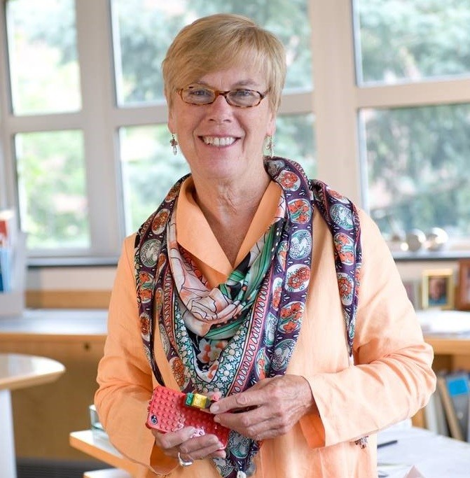 Woman wearing glasses, an orange blouse, a patterned scarf and a smile