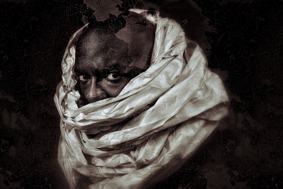 Artistic portrait of a person wrapped in flowing white fabric against a textured black background, creating a dramatic effect.