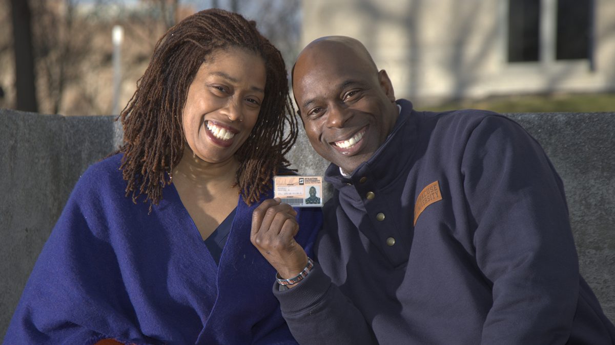 A wife and husband pose for a photo while sitting on a bench at Syracuse University.