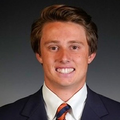 A student smiles while posing for a headshot in front of a grey backdrop.