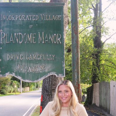 Katie Hannon stands in front of sign that reads Incorporated Village of Plandome Manor